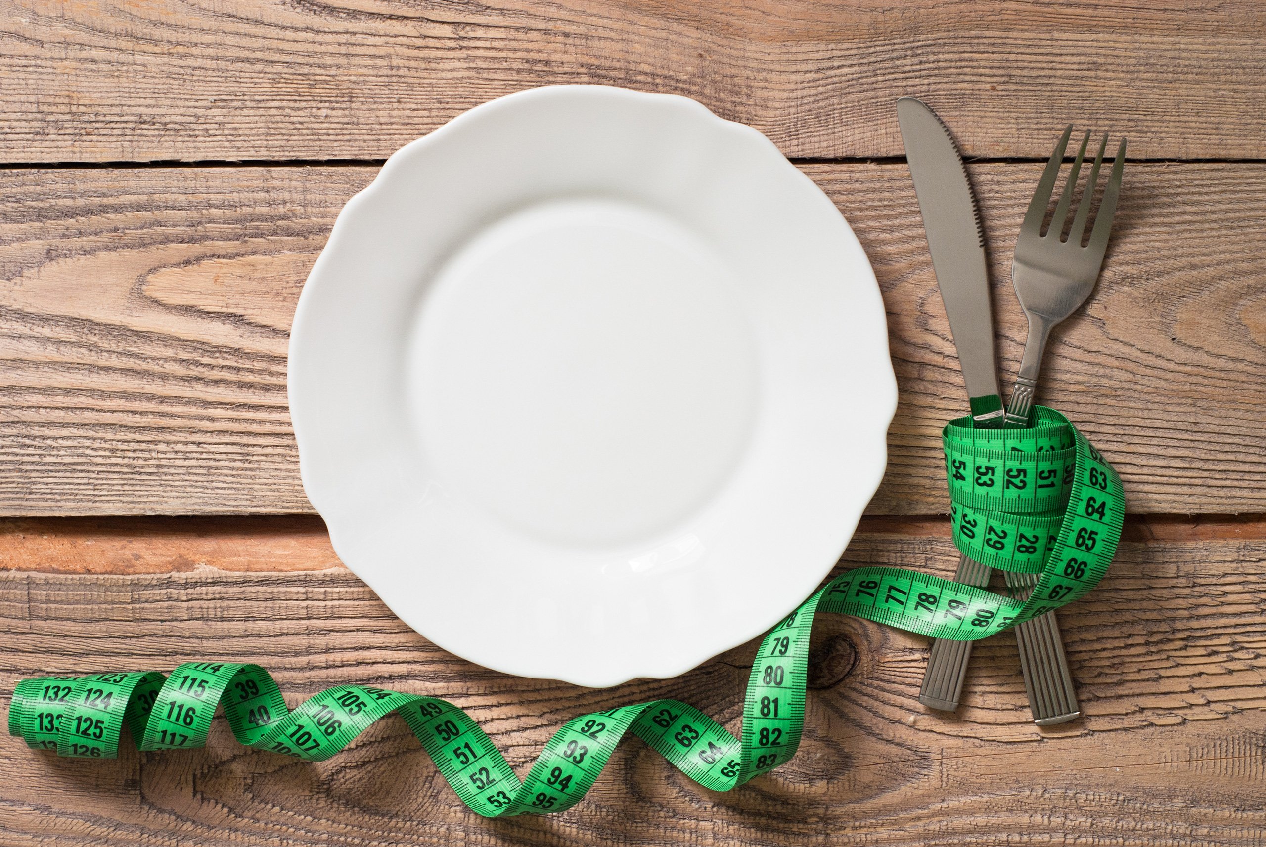 LaVie-weight-loss-center-omaha-2 empty white dinner plate on a wood table with a green measurement tape around a knife and a fork